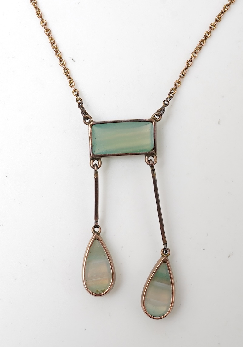 An Edwardian agate necklace, early 20th century, of negligée design, centring on a rectangular cabochon of translucent pale green agate, suspending a pair of pendants of unequal lengths, culminating in pear-shaped caboch